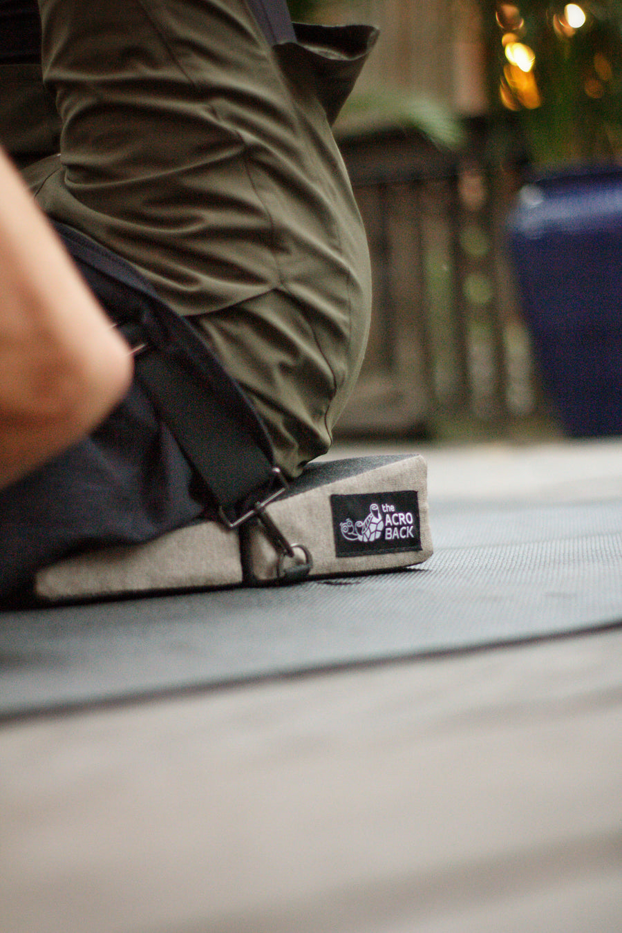 Close-up of The AcroBack Go wedge on AcroYoga mat showing branded turtle logo label and FastClasp strap hardware in use